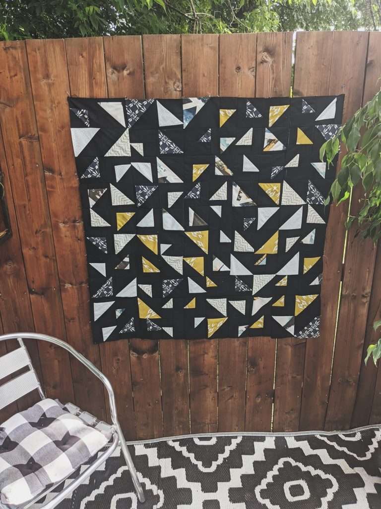 Baby Size Triangular Quilt with black background, yellow and neutral colored triangles